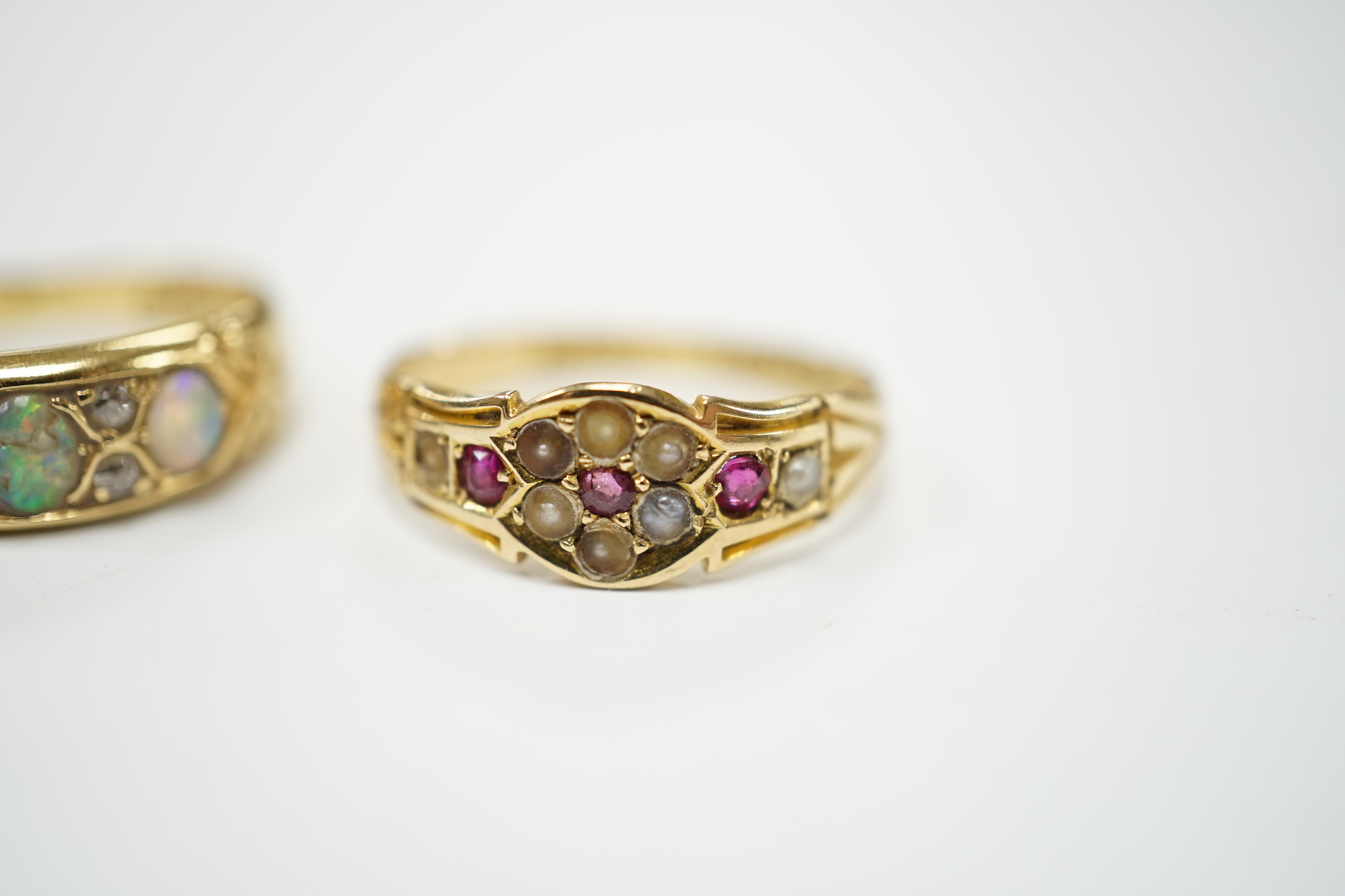 A late Victorian 18ct gold and three stone white opal set half hoop ring, with diamond chip spacers, size M (opal chipped), together with a similar 18ct gold, ruby and seed pearl ring, size K/L, gross weight 5.7 grams.